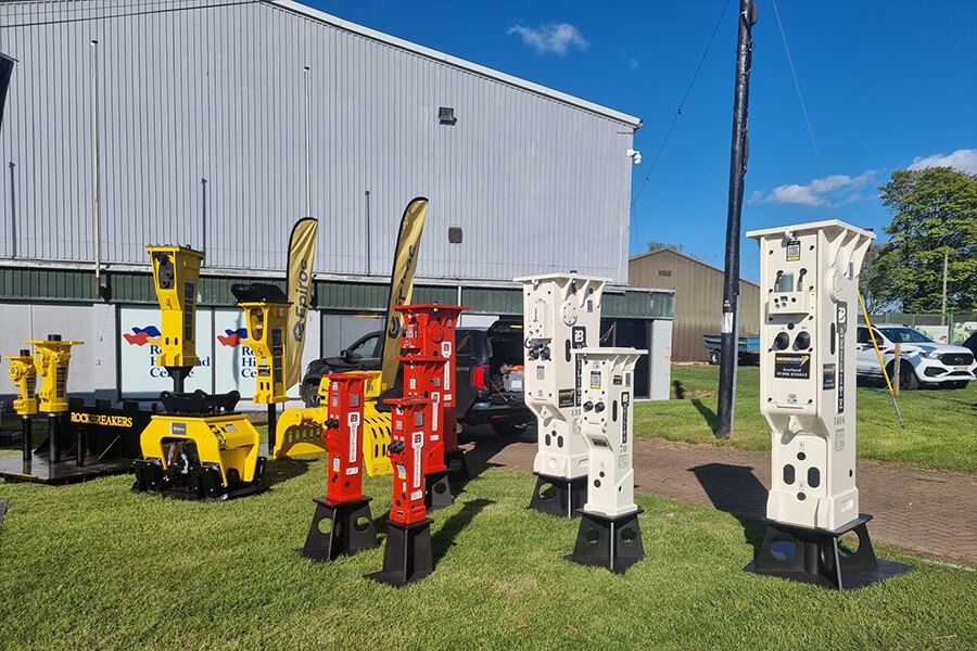hydraulic-breaker-model-is-placed-on-the-grass,-with-a-warehouse-in-the-background